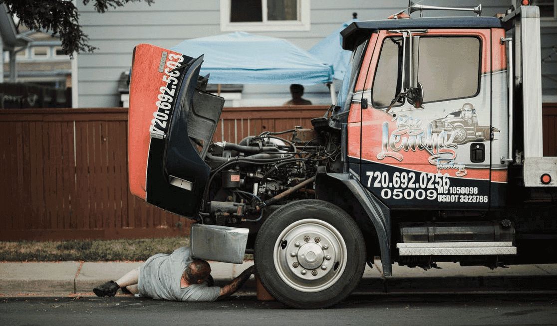Person fixing a truck on the road while lying under it